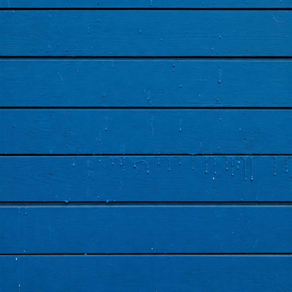 Blau gestrichene Holzfläche mit sichtbaren Farbnasen und Tropfen durch zu dick aufgetragene Farbe.