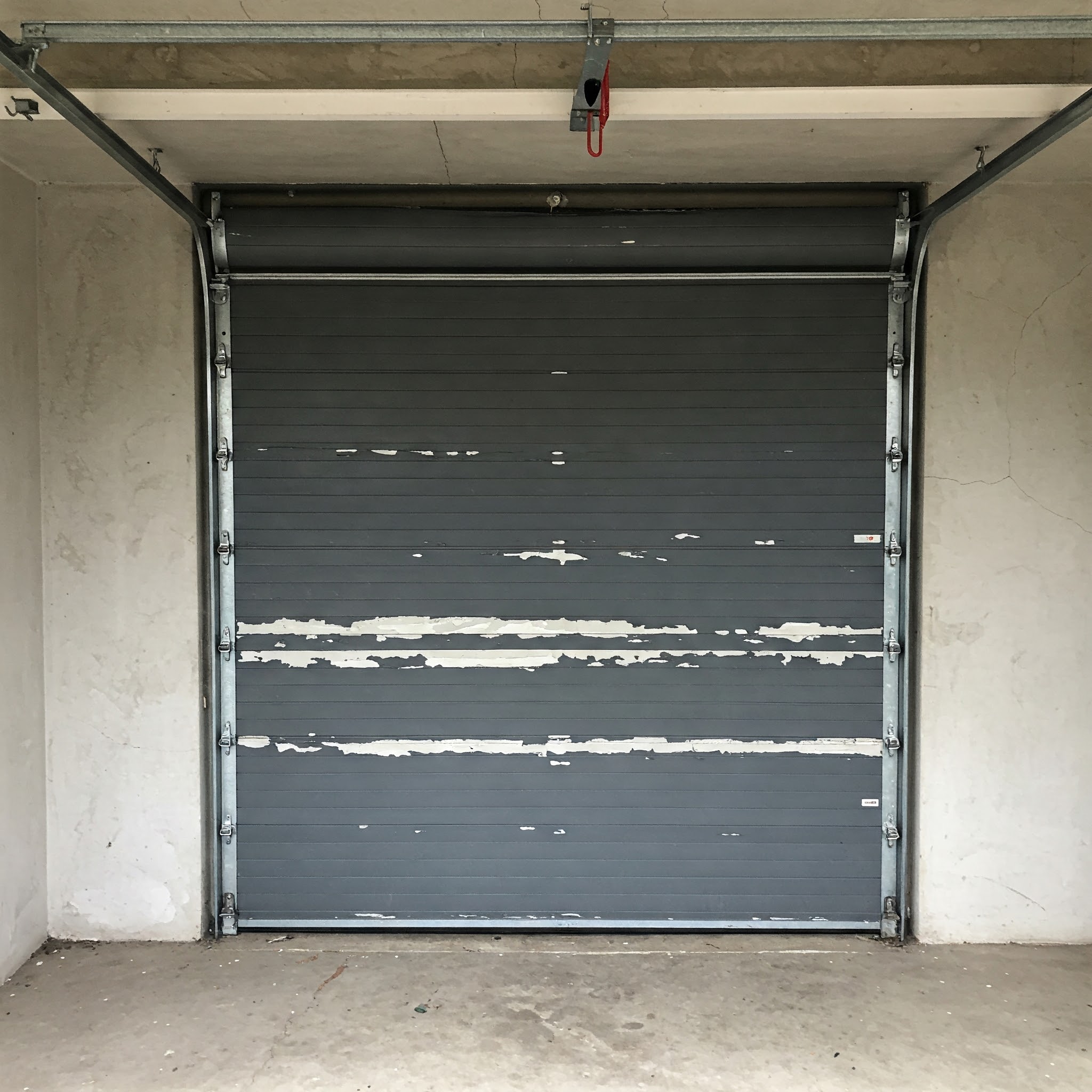 Garage mit grauem Kunststofftor, an dem die Farbe großflächig abblättert – deutlicher Hinweis auf fehlende Haftgrundierung.