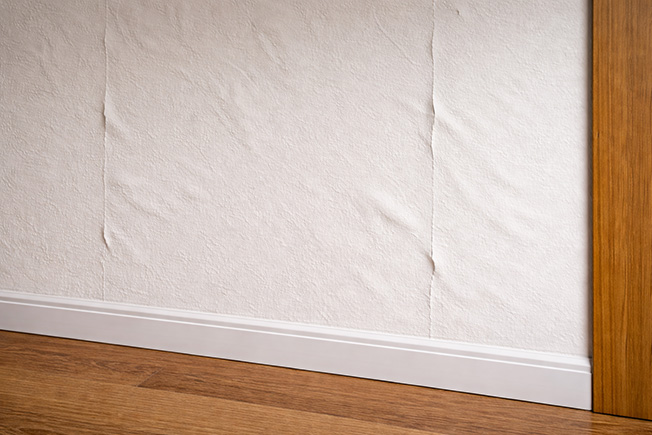 Überstrichene Tapete mit Wellen und sichtbaren Nähten durch Feuchtigkeit nach dem Streichen der Wand